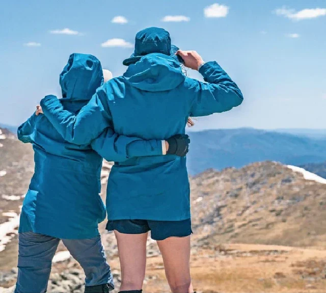Two people wearing blue coats facing the mountain