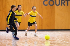 Three girls in yellow and black sportswear play indoor soccer, chasing a yellow ball