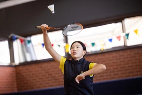 Student in a gym playing badminton, preparing to hit a shuttlecock with a racket
