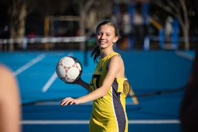 Girl in a yellow sports uniform holding a netball on an outdoor court, smiling