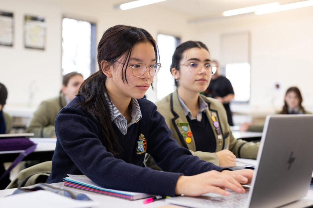 Two focused students working on a laptop during a classroom session.