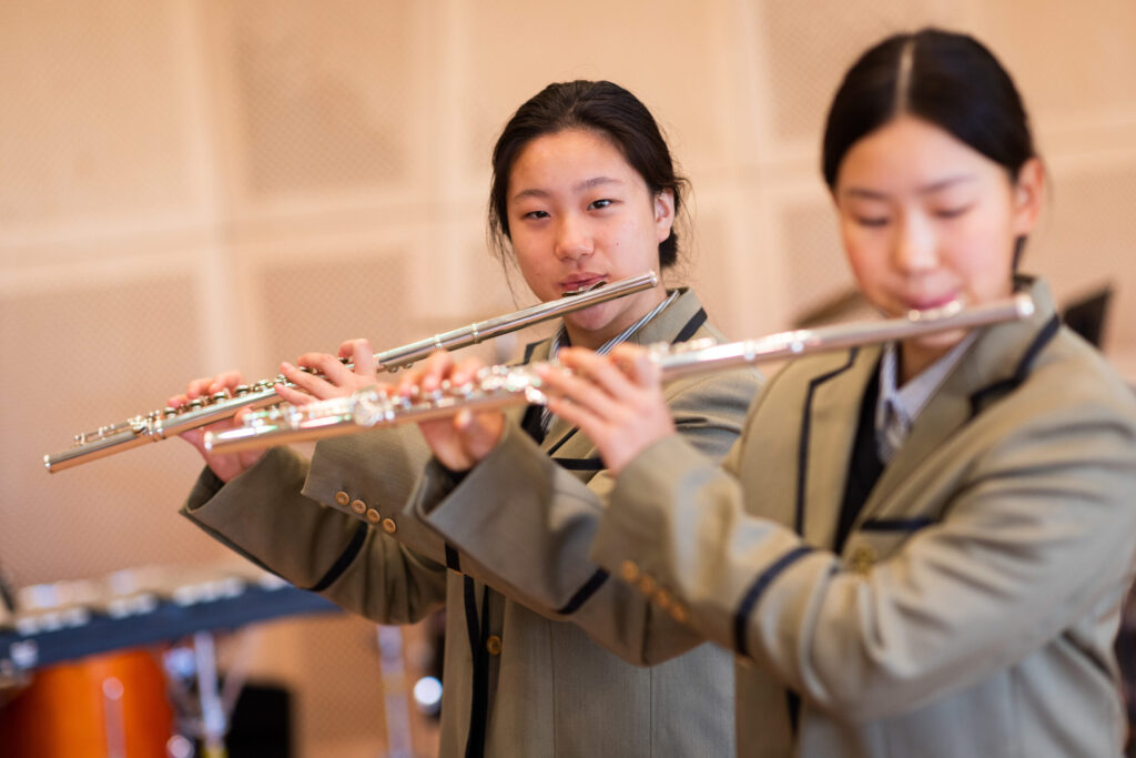 Two students in uniform playing flutes during a music performance or practice.